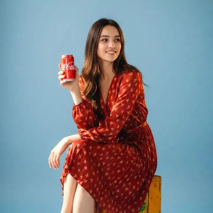 Улыбающаяся женщина поднимает красную банку Coca-Cola к камере на синем фоне. · пример 2