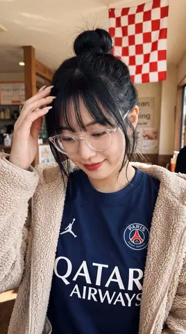 Женщина в джерси PSG и бежевой плюшевой куртке снимает селфи.