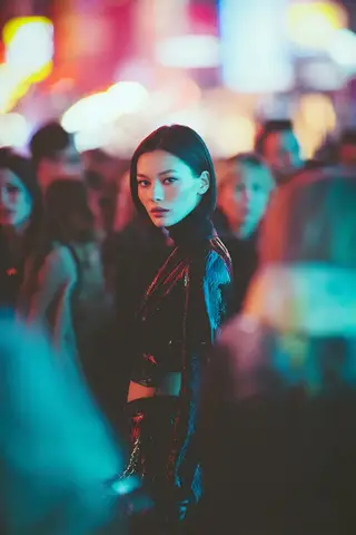 Стильная женщина с коротким каре стоит среди размытых людей и неоновых огней киберпанк-города.
