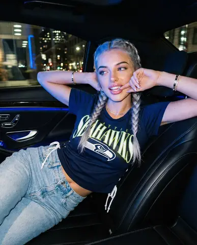 Женщина в одежде Seattle Seahawks лежит на заднем сиденье авто при синем неоновом свете
