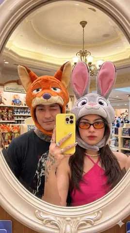 Мужчина и женщина фотографируются в овальном зеркале магазина Disney в шапках Nick Wilde и Judy Hopps.
