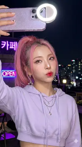 K-pop-исполнительница LUNA делает селфи на крыше кафе с неоновыми вывесками.