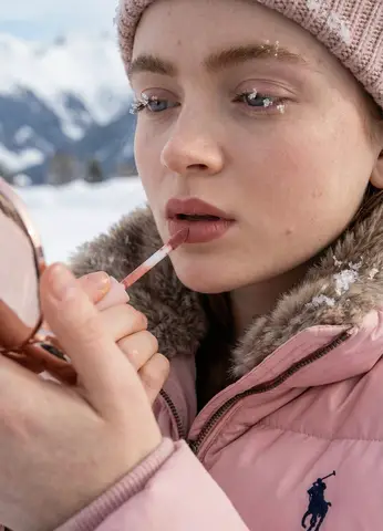 Девушка наносит помаду Kylie Cosmetics среди снега в Альпах.