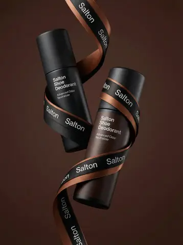 Две матовые бутылки Salton Shoe Deodorant парят в воздухе, соединённые чёрно-коричневой атласной лентой.