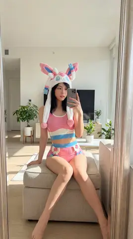 Джису из Blackpink в розово-бело-синем латексном образе Сильвеона сидит на пуфе в светлой комнате.