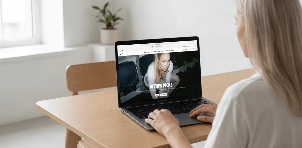 Женщина сидит за столом со спиной к камере и работает за MacBook.