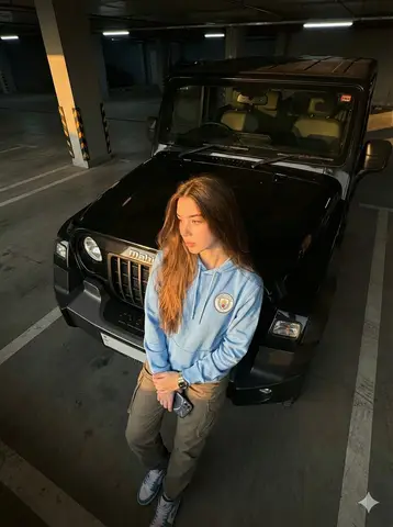 Женщина в голубом худи опирается на чёрный Mahindra Thar Roxx в гараже.