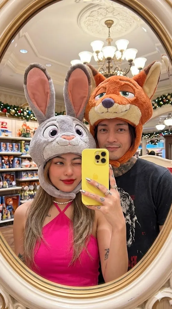 Мужчина и женщина фотографируются в овальном зеркале магазина Disney в шапках Nick Wilde и Judy Hopps. · пример 2