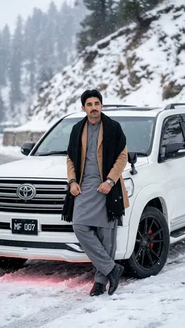 Мужчина в зимней одежде опирается на белый Land Cruiser на заснеженной горной дороге.