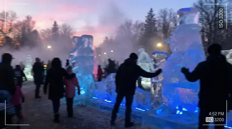 Люди среди ледяных скульптур в зимнем тумане при голубом свете.
