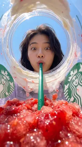 Молодой мужчина сверху заглядывает в стакан Starbucks с клубничным напитком и зелёной трубочкой.