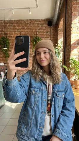 Молодая женщина делает вертикальное селфи на iPhone в современной уличной одежде.