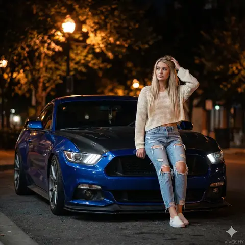 Молодая женщина позирует у синего Ford Mustang GT на ночной городской улице.