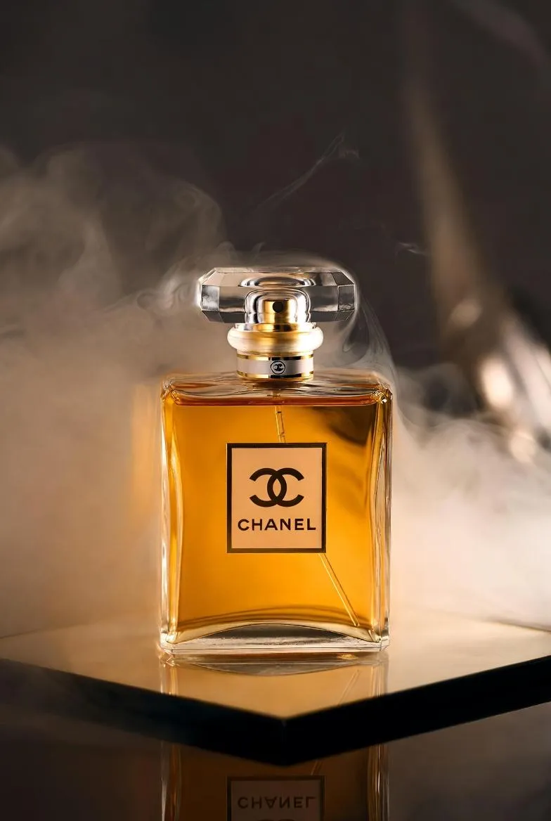 Флакон духов Chanel стоит на зеркальной поверхности в мягком тумане и тёплом свете. · пример 1