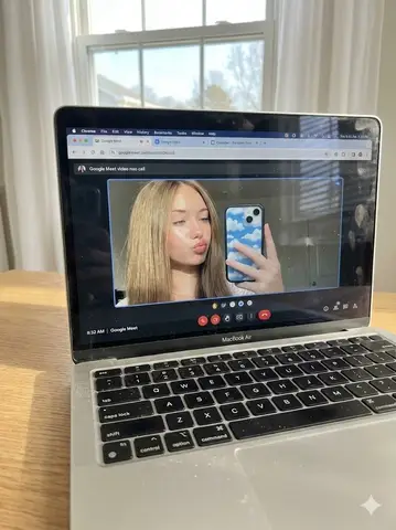 На экране серебристого MacBook Air открыт видеозвонок Google Meet с женщиной, которая делает селфи через веб-камеру.