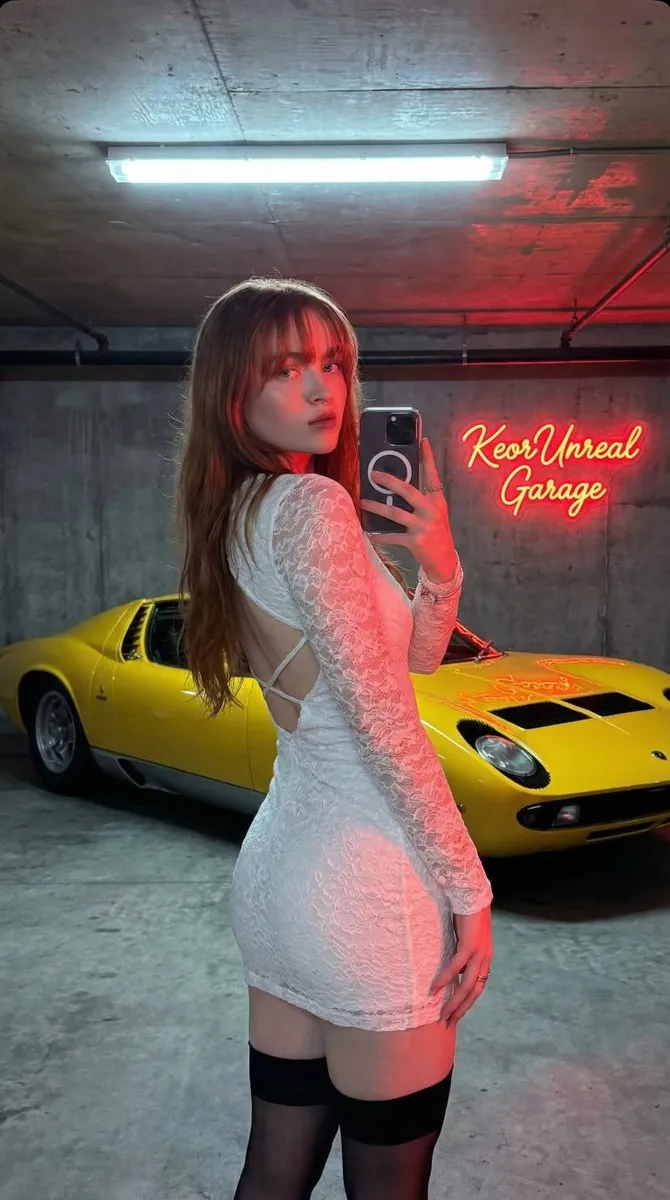 Женщина в чёрном платье делает селфи в гараже с красным Ferrari и вывеской KeorUnreal Garage. · пример 3