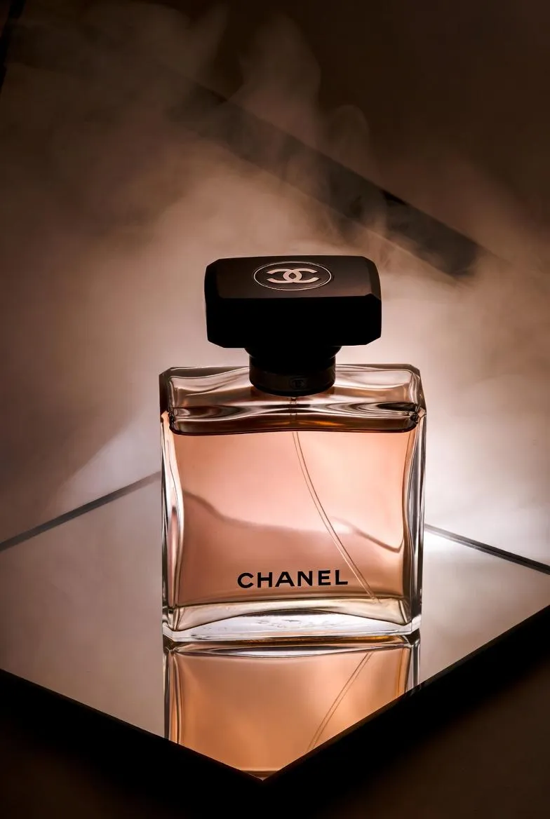 Флакон духов Chanel стоит на зеркальной поверхности в мягком тумане и тёплом свете. · пример 3